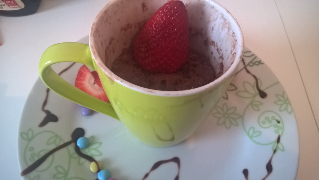 Ein Mikrowellenrezept. In einer Tasse ist frischer Schokoladenkuchen. Mit einer Erdbeere garniert. 