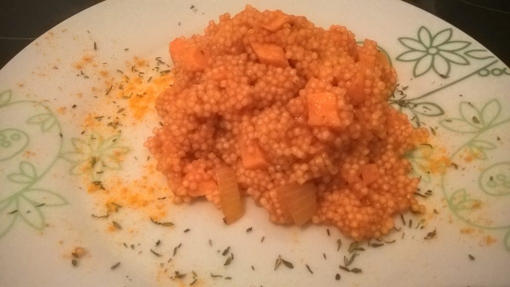 Tomaten-Süßkartoffel-Couscous auf einem Teller. Dekoriert mit Kräutern. Wenn man auf das Bild klickt gelangt man zum eiweißarmen Rezept für Menschen mit PKU.