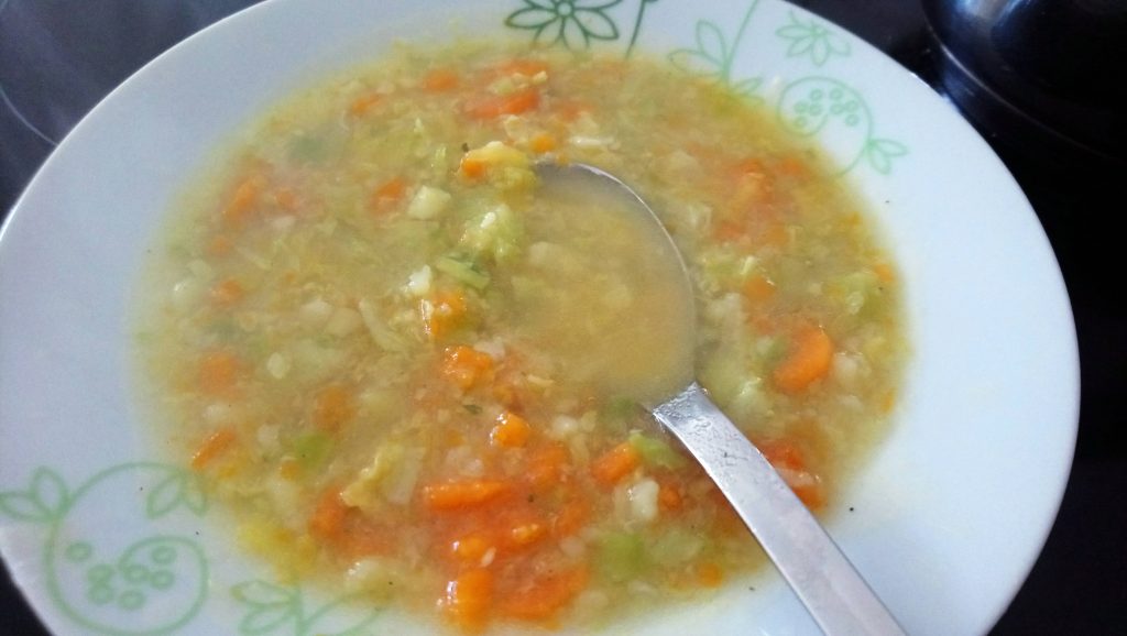 Ein Teller mit leckerer Gemüsesuppe. Ein Löffel liegt schon in der Suppe bereit. Wenn man auf das Bild klickt gelangt man zum eiweißarmen Rezept für Menschen mit PKU.