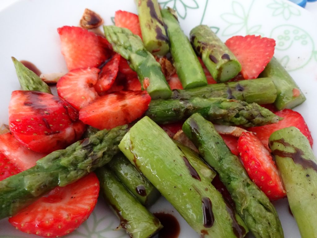Auf einem Teller liegen als Salat gemischt grüner Spargel und Erdbeeren. Alles ist mit Balsamico-Dressing überträufelt. Wenn man auf das Bild klickt gelangt man zum eiweißarmen Rezept für Menschen mit PKU.