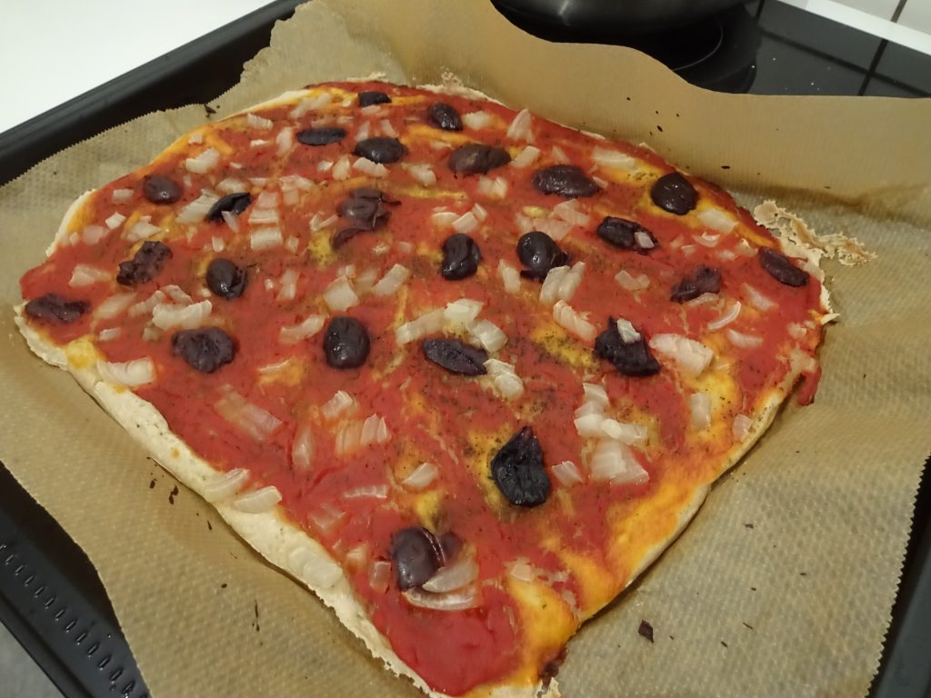 Ein Backblech mit einer Pizza darauf. Die Pizza hat Oliven und Zwiebeln als Belag. Wenn man auf das Bild klickt gelangt man zum eiweißarmen Rezept für Menschen mit PKU.